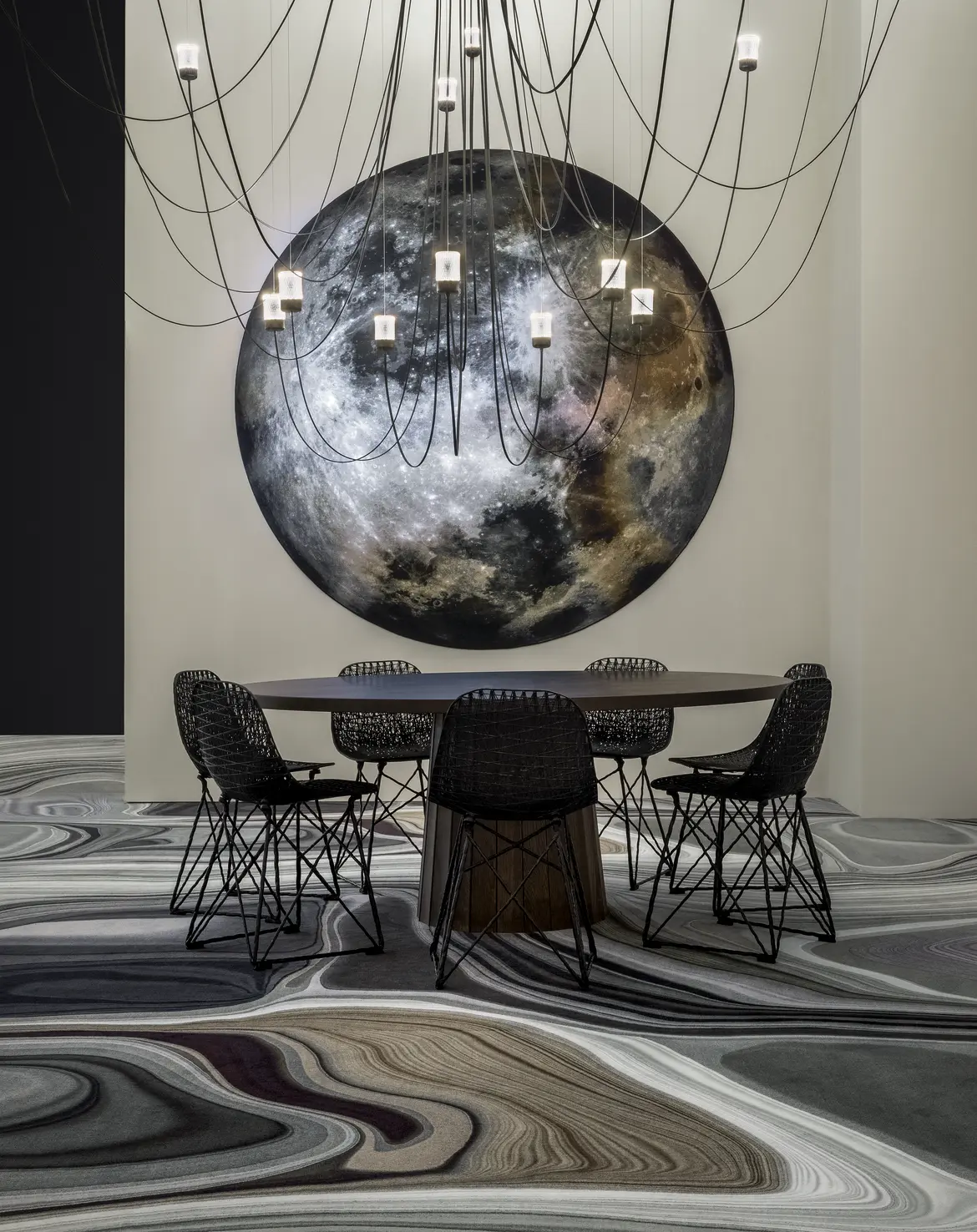 mooon carpet on the wall with gravity chandelier and container table setting with carbon chairs